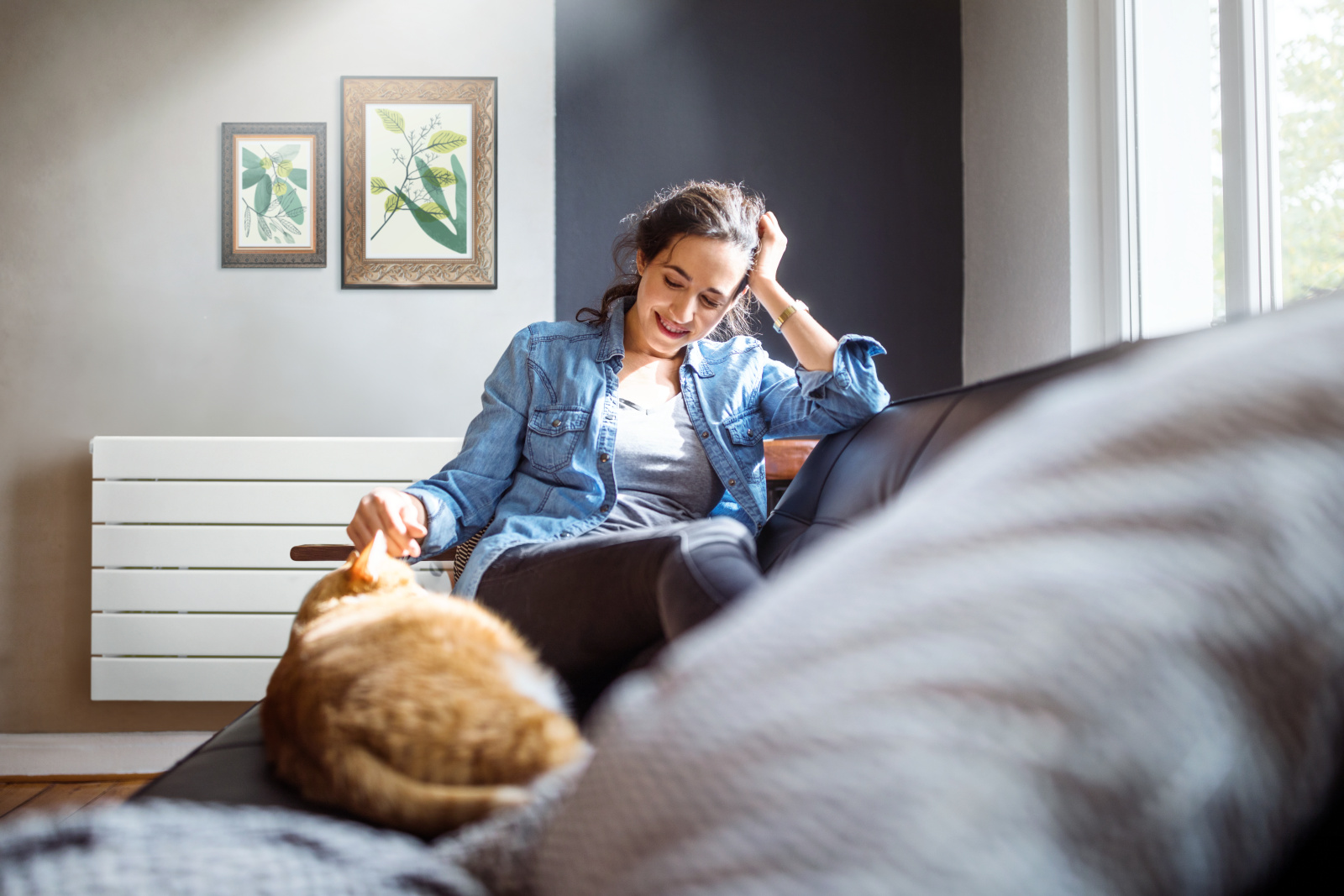 Beautiful young woman relaxing on sofa with her cat in living room.